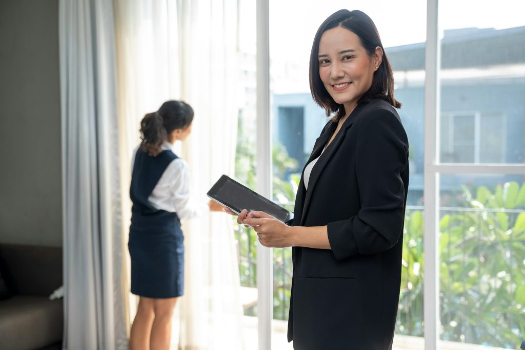 Housekeeping manager working on digital tablet and controlling the work of staff in the hotel room.